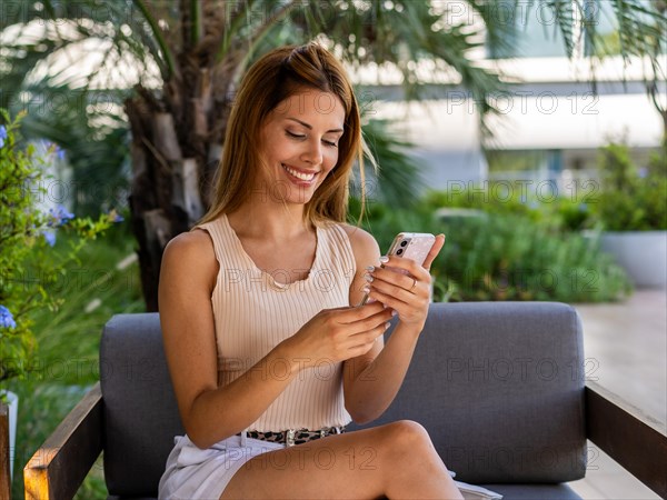 Smiling woman is sitting on a sofa while she turns off her smartphone