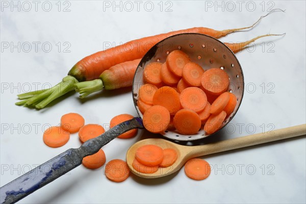 Carrot slices in colander and wooden spoon, Daucus carota