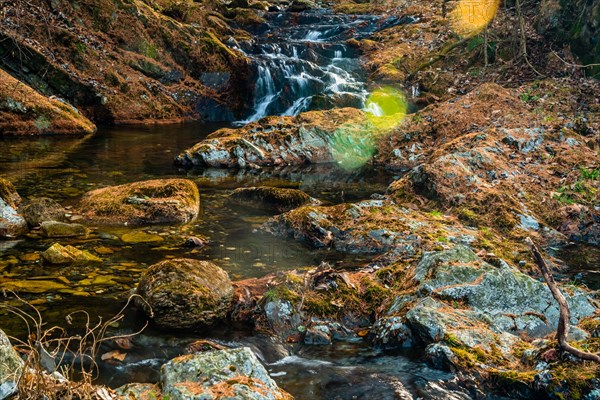 A waterfall with motion blur flows through rocks surrounded by autumn foliage, in South Korea