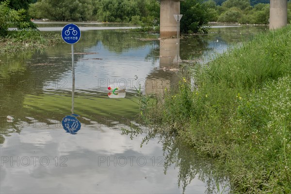 Round sign says BICYCLE PATH in Korean, with trees submerged in flooded river after torrential monsoon rains in Daejeon South Korea