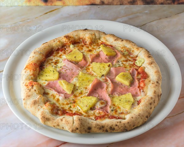 Tropical Hawaiian pizza with pineapple slices and ham on a baked dough base served whole with copyspace, pizza