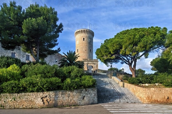 A robust stone castle tower surrounded by lush greenery under a blue sky, Palma De Mallorca