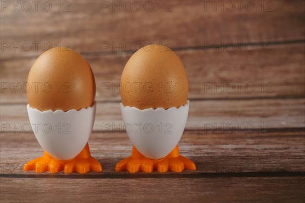 Two fresh eggs in an egg cup in the shape of a chicken on a wooden table
