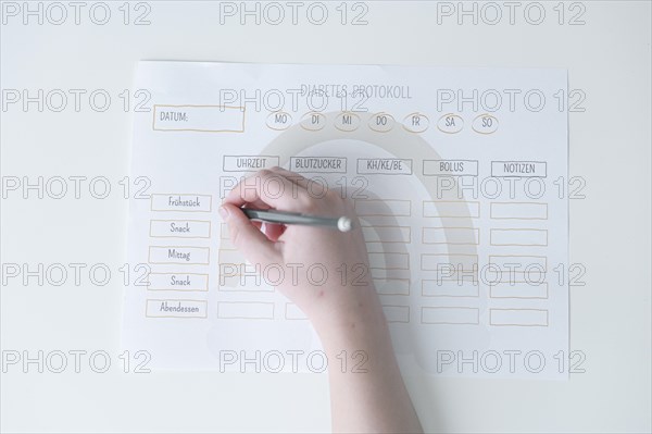 Diabetes log, daily log of food and insulin administration, food log, hand of a child holding a pen and appearing to fill in the log, the paper lies on a white table, Ruhr area, Germany, Europe