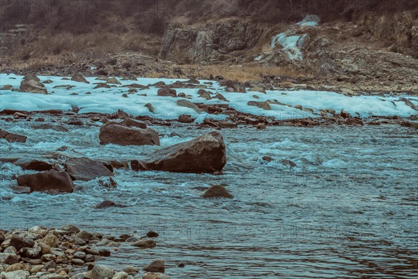 Dynamic river with scattered rocks and patches of ice on a cloudy winter day, in South Korea