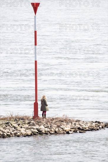 A person next to a red and white lighthouse sign on the bank of a calm river