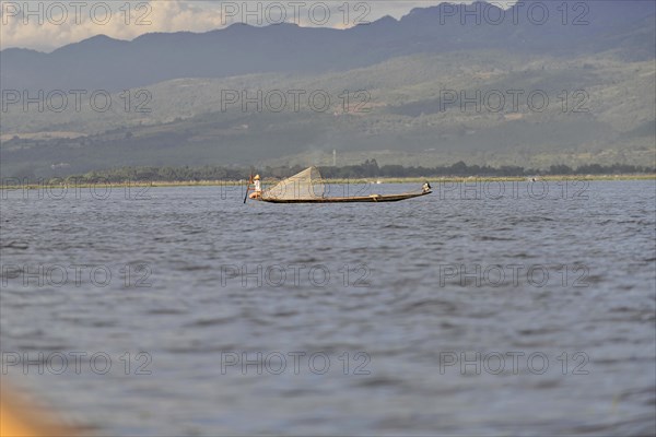 Lone fisherman on a boat pulling a net in calm waters, Inle Lake, Myanmar, Asia