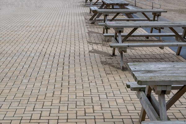 Empty wooden picnic tables arranged on a stone-paved floor, Zeebrugge, Flanders, Belgium, Europe