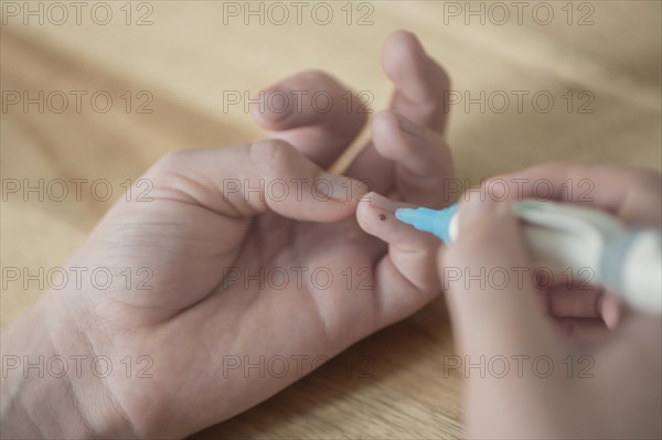 On the left a child's hand with a drop of blood on the little finger, in the right hand the child holds the lancet, lancing device, has just pricked himself, wooden table as background, blood glucose measurement, diabetes treatment, glucose measurement, Ruhr area, Germany, Europe