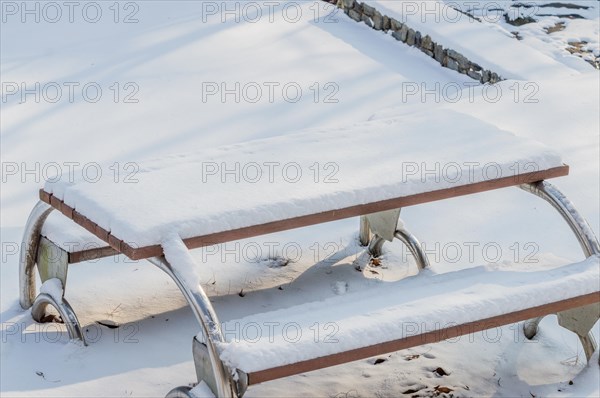 A wooden bench with metal framework covered in a thick layer of snow, in South Korea