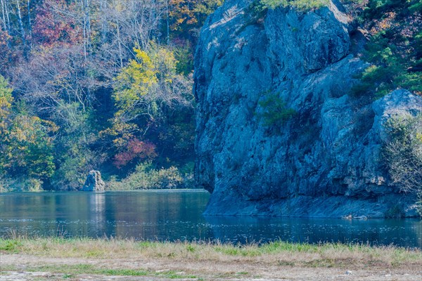 Rock faces with autumnal trees reflected in a calm lake creating a peaceful landscape, in South Korea