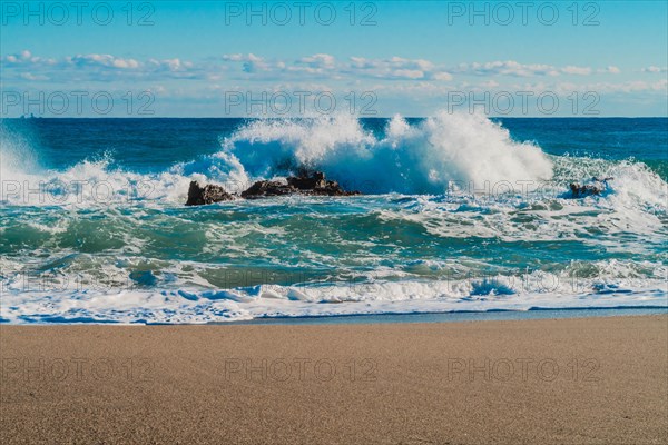Waves crash energetically against rocks at the beach under a bright blue sky, in South Korea