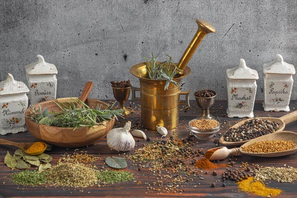 Antique spice containers and a mortar surrounded by fresh herbs and spices on a wooden surface