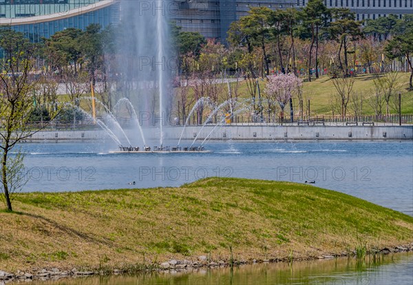 Fountain with water jets in a lake at a park with city skyline in background, in South Korea
