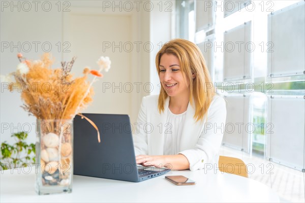 Portrait in the office of a female beauty real estate agent working using laptop and smiling