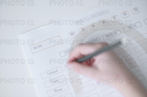 Diabetes log, daily log of food and insulin administration, food log, hand of a child holding a pen and appearing to fill in the log, the paper lies on a white table, Ruhr area, Germany, Europe