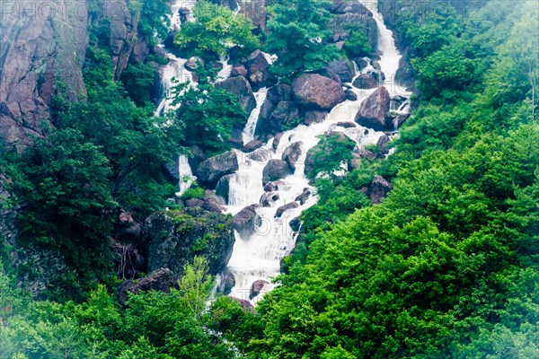 Rocky waterfall with multiple cascades amidst a dense green forest, in South Korea