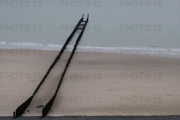 A breakwater extends into the sea on an empty sandy beach in calm seas