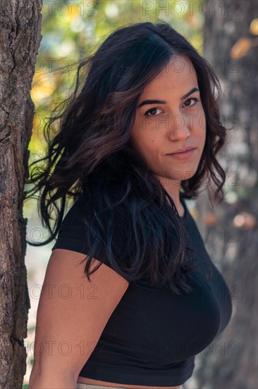 Outdoor shot of a Cheerful hispanic young sexy woman with a powerful stance and confident gaze, wearing a black shirt, selective focus, blurred background with bokeh, daytime, AI generated