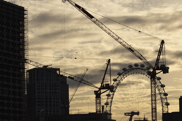 London Eye or Millennium Wheel tourist observation wheel at sunsetwith industrial cranes and cityscape in the foreground, City of London, England, United Kingdom, Europe