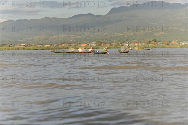 Fishing boats glide across the water with mountains in the background, Inle Lake, Myanmar, Asia