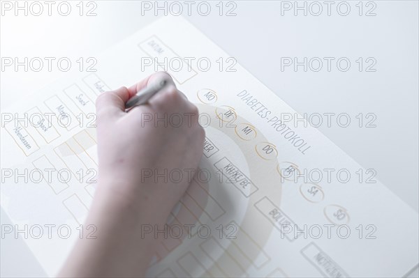 Diabetes log, daily log of food and insulin administration, food log, hand of a child holding a pen and appearing to fill in the log, the paper lies on a white table, Ruhr area, Germany, Europe