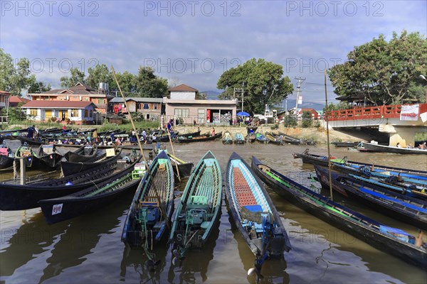 View of calm waterway with anchored boats, a bridge in the background and surrounding houses, Inle Lake, Myanmar, Asia