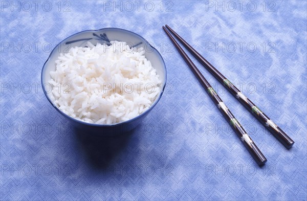 A blue bowl of white rice with chopsticks on a textured blue background