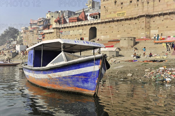 Abandoned boat in the foreground with a view of polluted river ghats, Varanasi, Uttar Pradesh, India, Asia