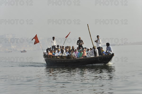 Group of passengers on a boat on a river, with a ferryman steering with a long oar, Varanasi, Uttar Pradesh, India, Asia