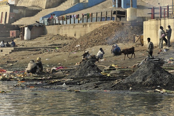 Riverbank with people and animals, surrounded by rubbish and smoke, creating a hazy atmosphere, Varanasi, Uttar Pradesh, India, Asia