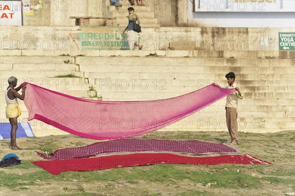 Two people helping to hang colourful laundry on a sunny riverbank, Varanasi, Uttar Pradesh, India, Asia