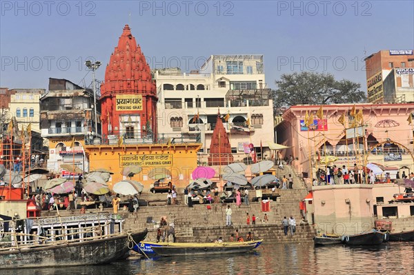 Red temples dominate the ghats by the river, surrounded by people and umbrellas, Varanasi, Uttar Pradesh, India, Asia