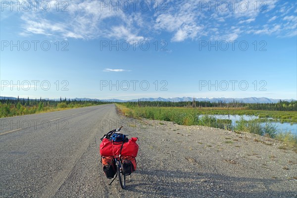 Bicycle standing on an endless straight road in the wilderness, bicycle tour, adventure trip, late summer, Alaska Highway, Yukon TerritoryCanada