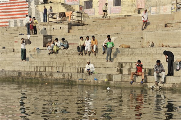 Group of people sitting and interacting by the ghats of a river in an urban environment, Varanasi, Uttar Pradesh, India, Asia