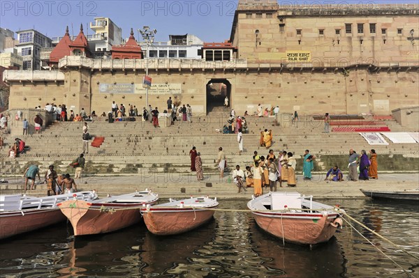 People walking on stairs along a river with docked boats, Varanasi, Uttar Pradesh, India, Asia