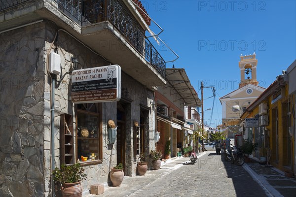 A traditional bakery on a alleyway corner with characteristic stone architecture under a blue sky, alley in old town with church, Koroni, Pylos-Nestor, Messinia, Peloponnese, Greece, Europe