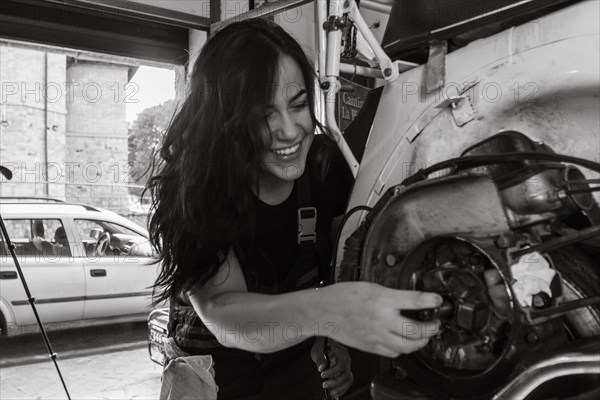 A cheerful female mechanic works on a moped italian vintage scooter motorcycle engine in a workshop, real women performing traditional man jobs of the past, black and white photograph