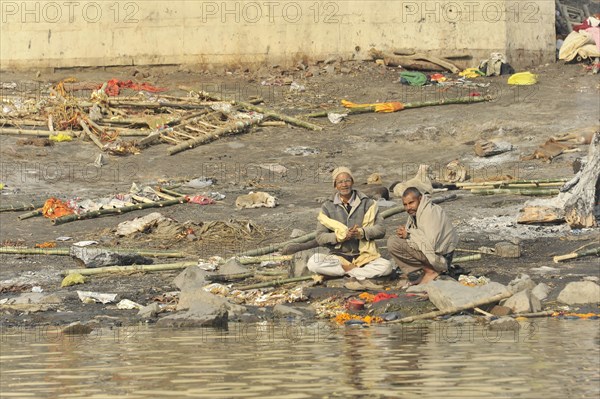 Two people sitting on the polluted bank of a river and seem to be engaged in a conversation, Varanasi, Uttar Pradesh, India, Asia