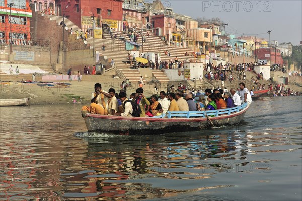 Filled boat with passengers on a river, city in the background, Varanasi, Uttar Pradesh, India, Asia
