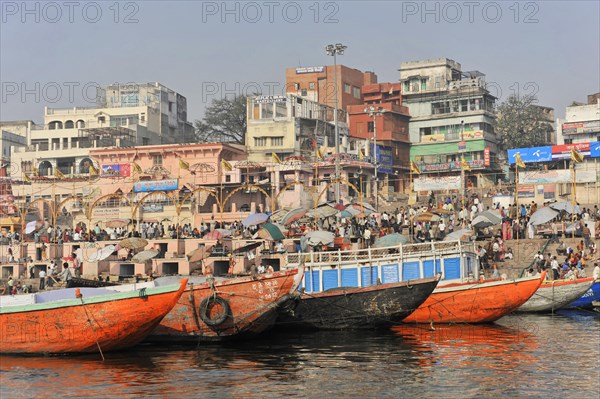 Colourful boats and hustle and bustle on the riverbank against an urban backdrop, Varanasi, Uttar Pradesh, India, Asia