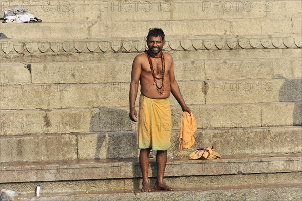 A smiling man in traditional dress stands on the ghats on the riverbank, Varanasi, Uttar Pradesh, India, Asia