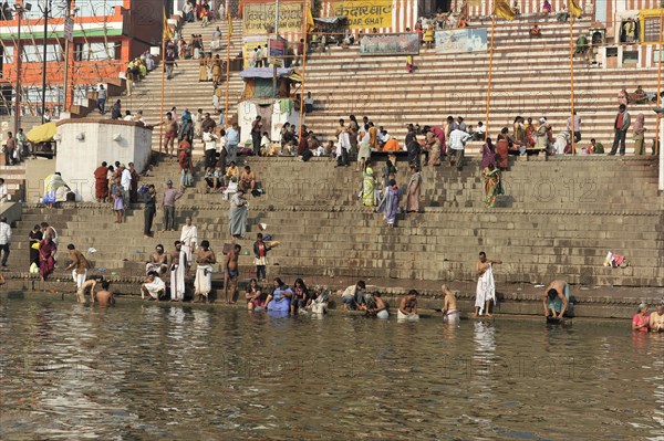 People on the steps of a river bank in a city, buildings in the background, Varanasi, Uttar Pradesh, India, Asia