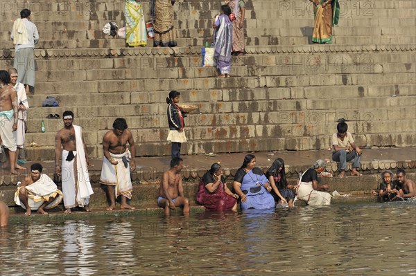 People in traditional clothing on river steps, partly in meditating posture while bathing, Varanasi, Uttar Pradesh, India, Asia