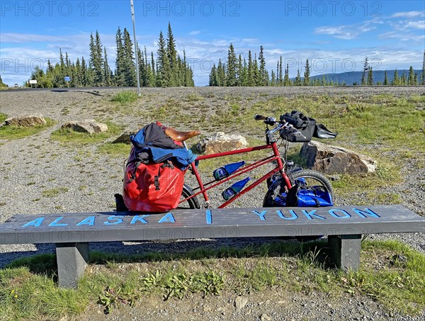 Bench right on the border between Alaska and the Yukon, packed touring bike, adventure travelling, Alaska Highway, Yukon Territory, Canada, North America