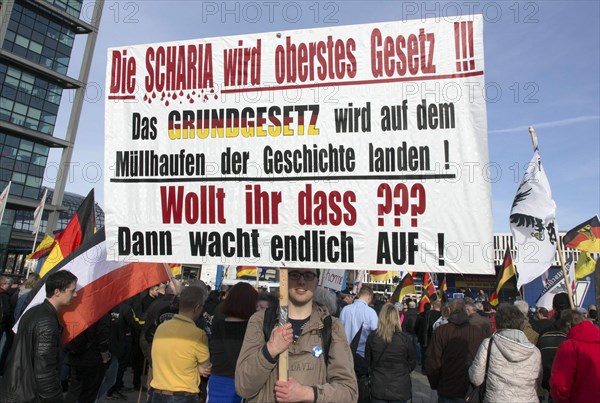 A participant in the Merkel muss weg demonstration holds a poster with the inscription Die Scharia wird oberstes Gesetz. Demonstration by right-wing populist and far-right participants, including supporters of the NPD, Pegida, Reichsbuerger, hooligans, Landsmannschaften and Identitarians, Berlin, 4 March 2017
