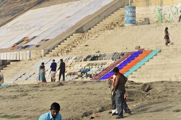 People walking and standing on a riverbank with stairs and colourful murals, Varanasi, Uttar Pradesh, India, Asia