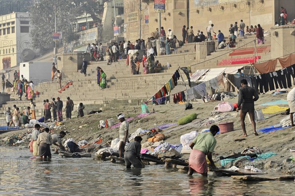 Lively scene by a river with people washing clothes and relaxing, Varanasi, Uttar Pradesh, India, Asia