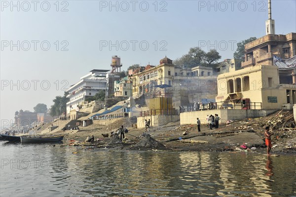 Urban riverbank with people living everyday life, framed by a culturally rich urban landscape, Varanasi, Uttar Pradesh, India, Asia