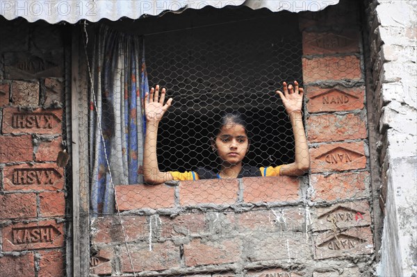 Young girl looking thoughtfully out of a window with brick surround, Varanasi, Uttar Pradesh, India, Asia